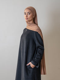 femme portant un manteau long noir avec un hijab beige, représentant un style élégant et moderne.