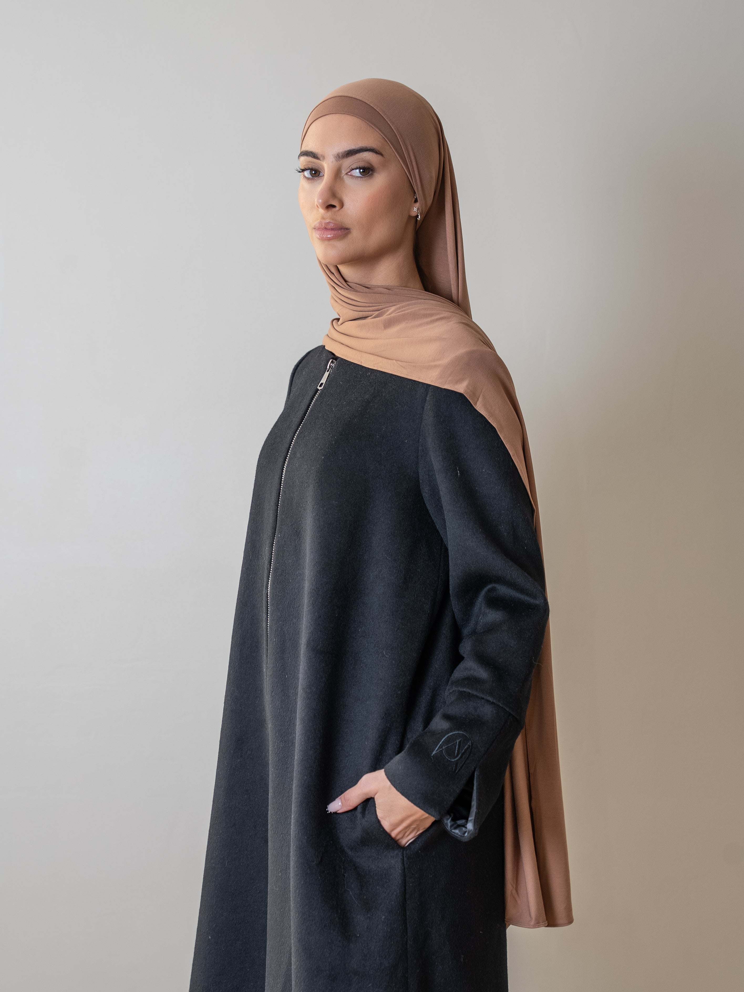 femme portant un manteau long noir avec un hijab beige, représentant un style élégant et moderne.
