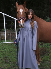 Femme portant un trench gris près d'un cheval, illustrant le style élégant et polyvalent du Trench.