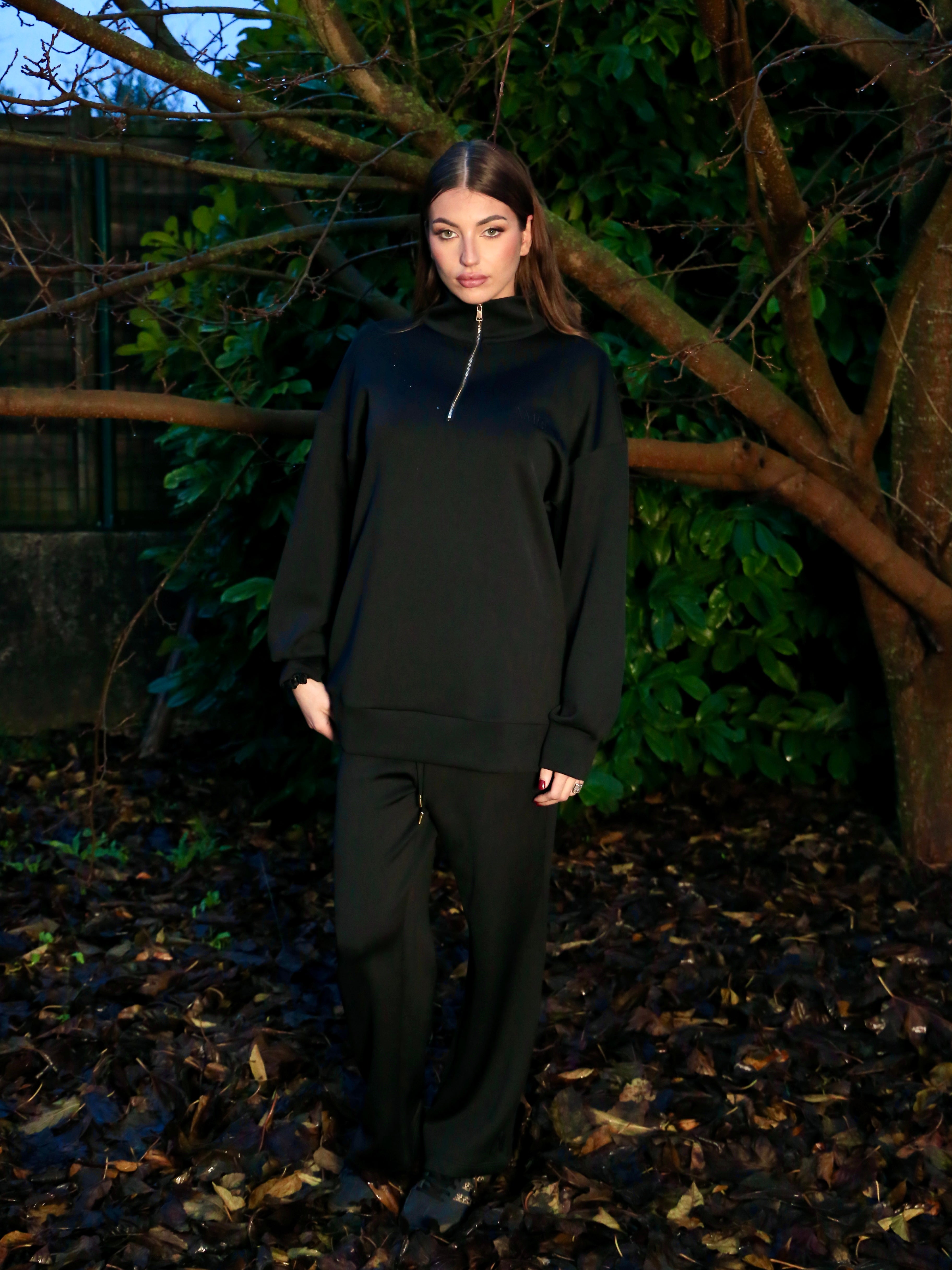 Ensemble jogging Naya en TENCEL™, femme portant un ensemble noir au près d'un arbre.